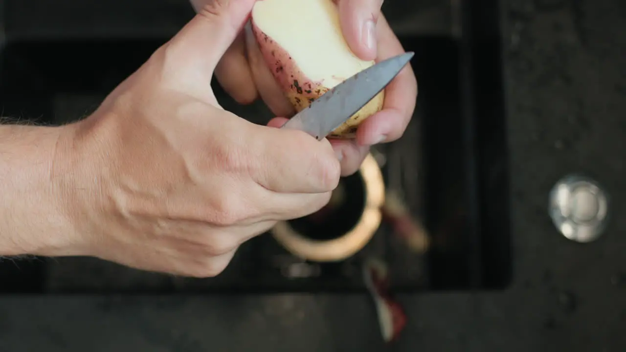 Man peels potatoes under running water from a kitchen faucet