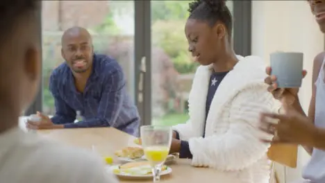 Young Daughter Butters a Croissant During Family Breakfast