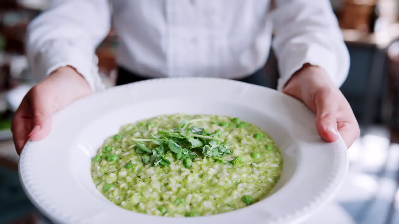 Close Up Of Restaurant Waitress Holding Plate Of Pea Risotto