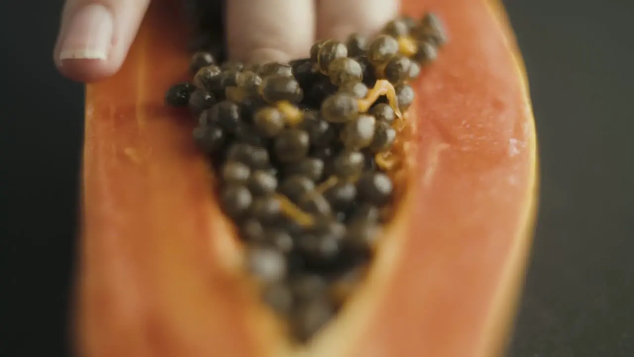 Close up of female fingers diving into the seeds of papaya cut in half