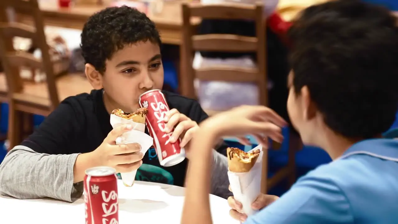 Two Arab Boys Eating Fast Food Meal With Softdrinks In Cans medium shot