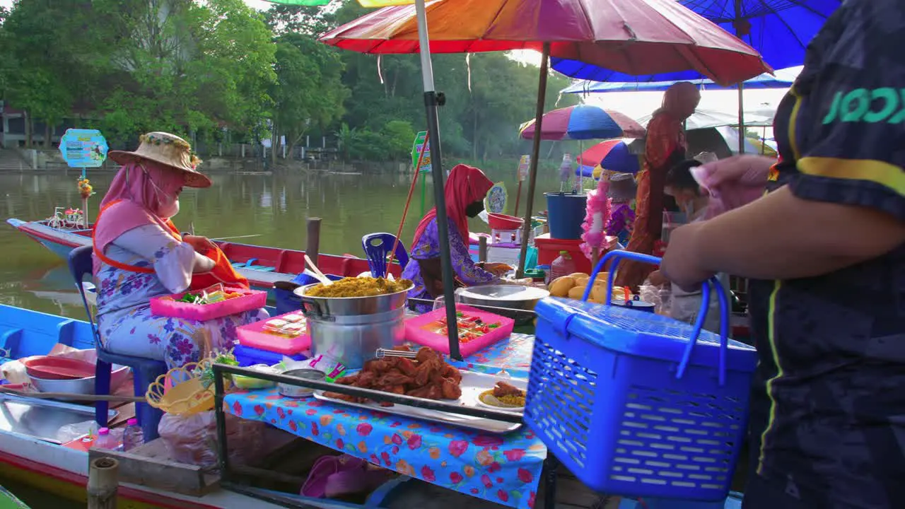 Thai woman worker selling local Asian food from a boat on the shores of a floating market