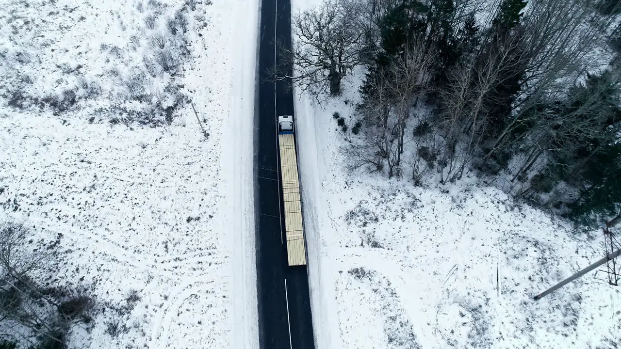 Isolated long truck loaded with lumber driving slowly along snowy road