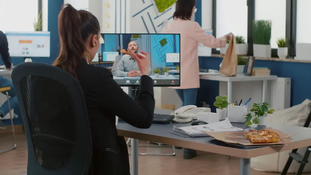 Executive manager eating pizza slice discussing with remote collegue during online videocall meeting