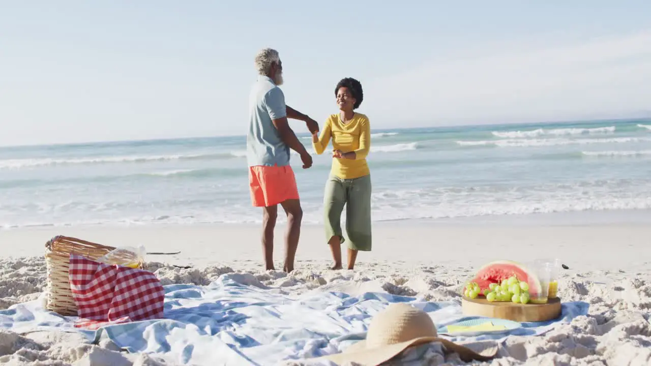 Happy african american couple having picnic and dancing on sunny beach