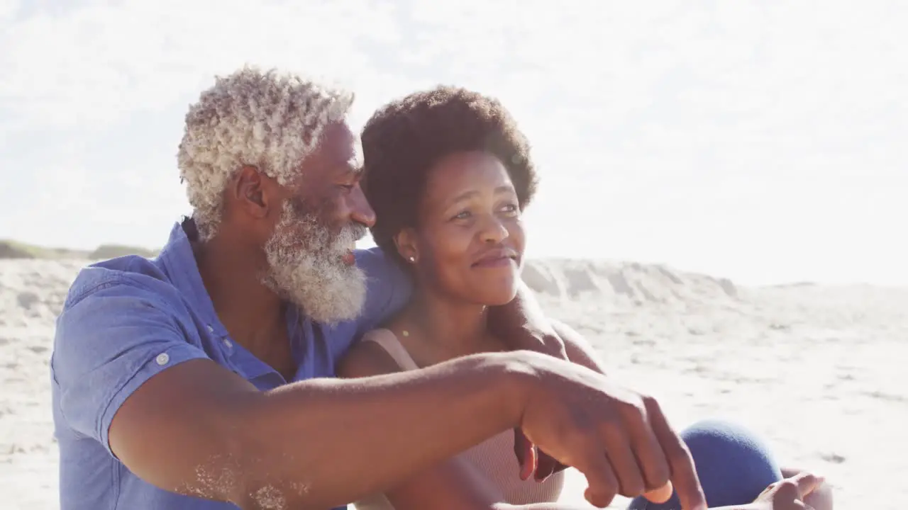 Happy african american couple sitting and embracing on sunny beach