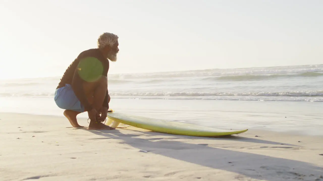 Senior african american man preparing before surfing on sunny beach