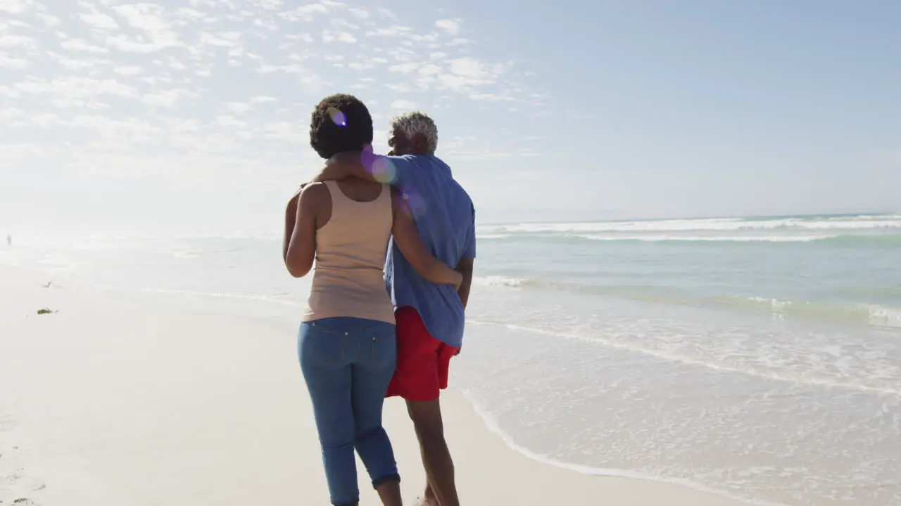 Happy african american couple walking and embracing on sunny beach