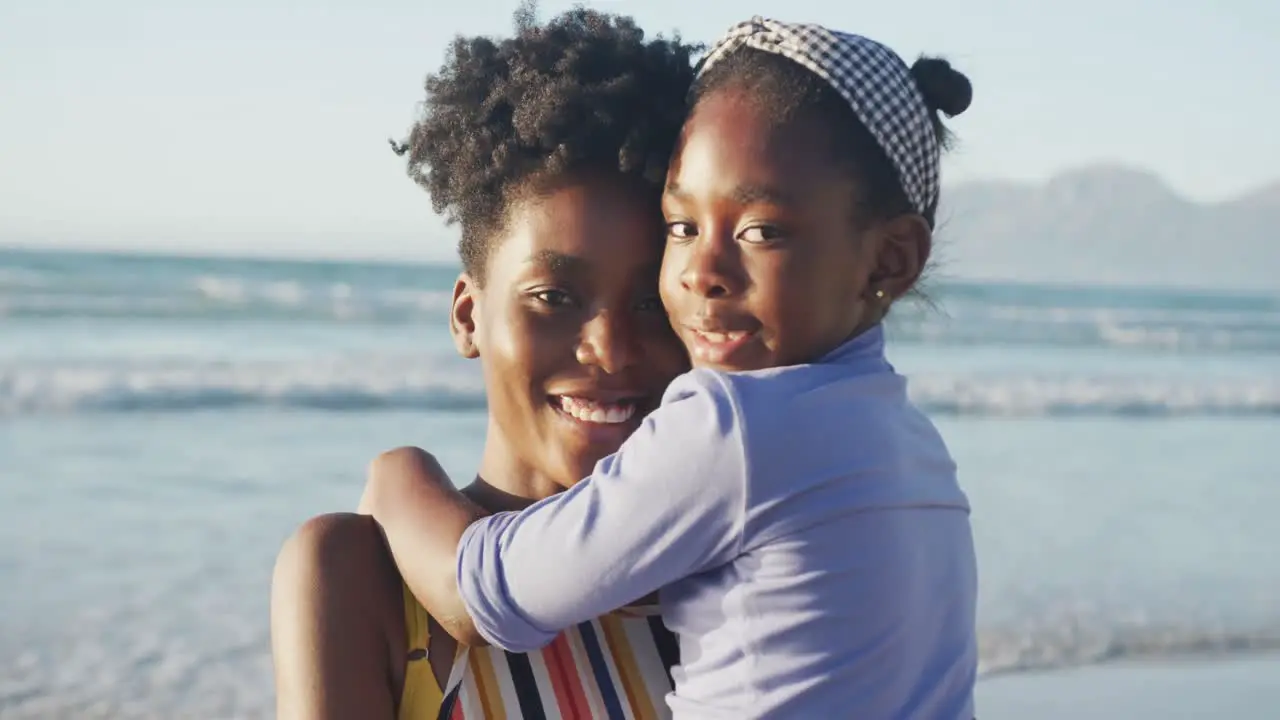 Portrait of happy african american mother embracing daughter on sunny beach