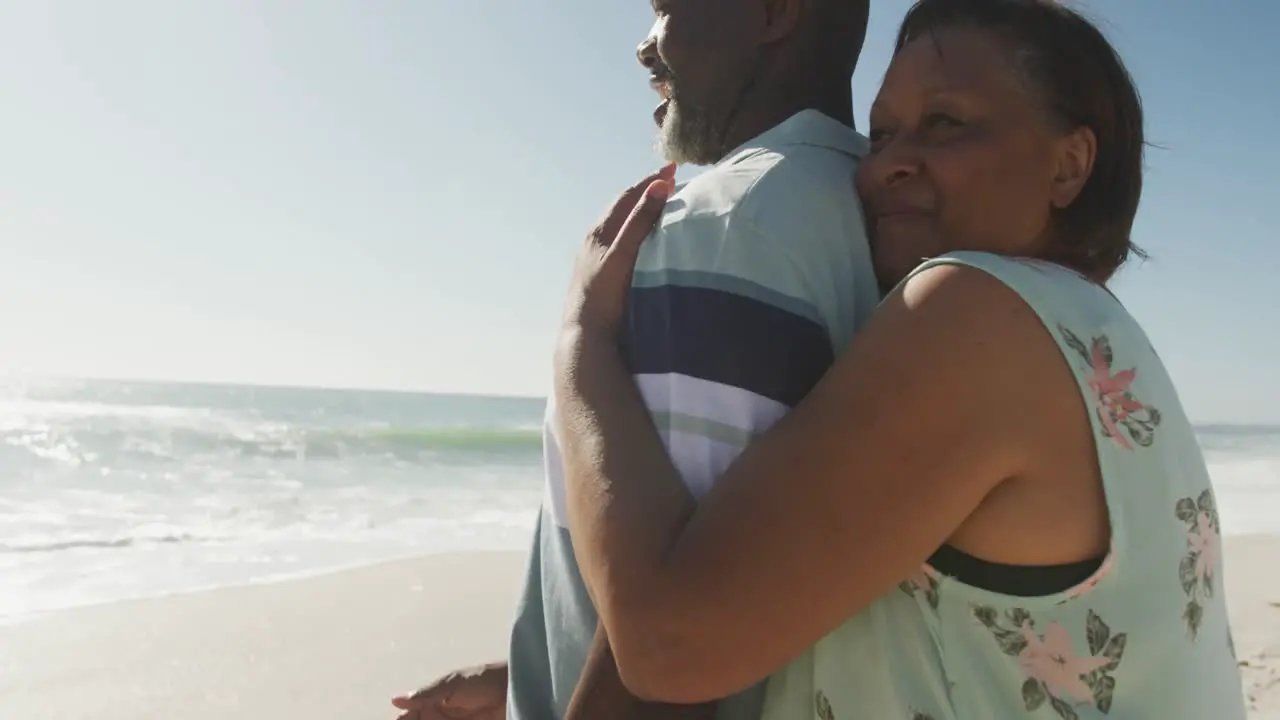 Smiling senior african american couple embracing and looking at sea on sunny beach