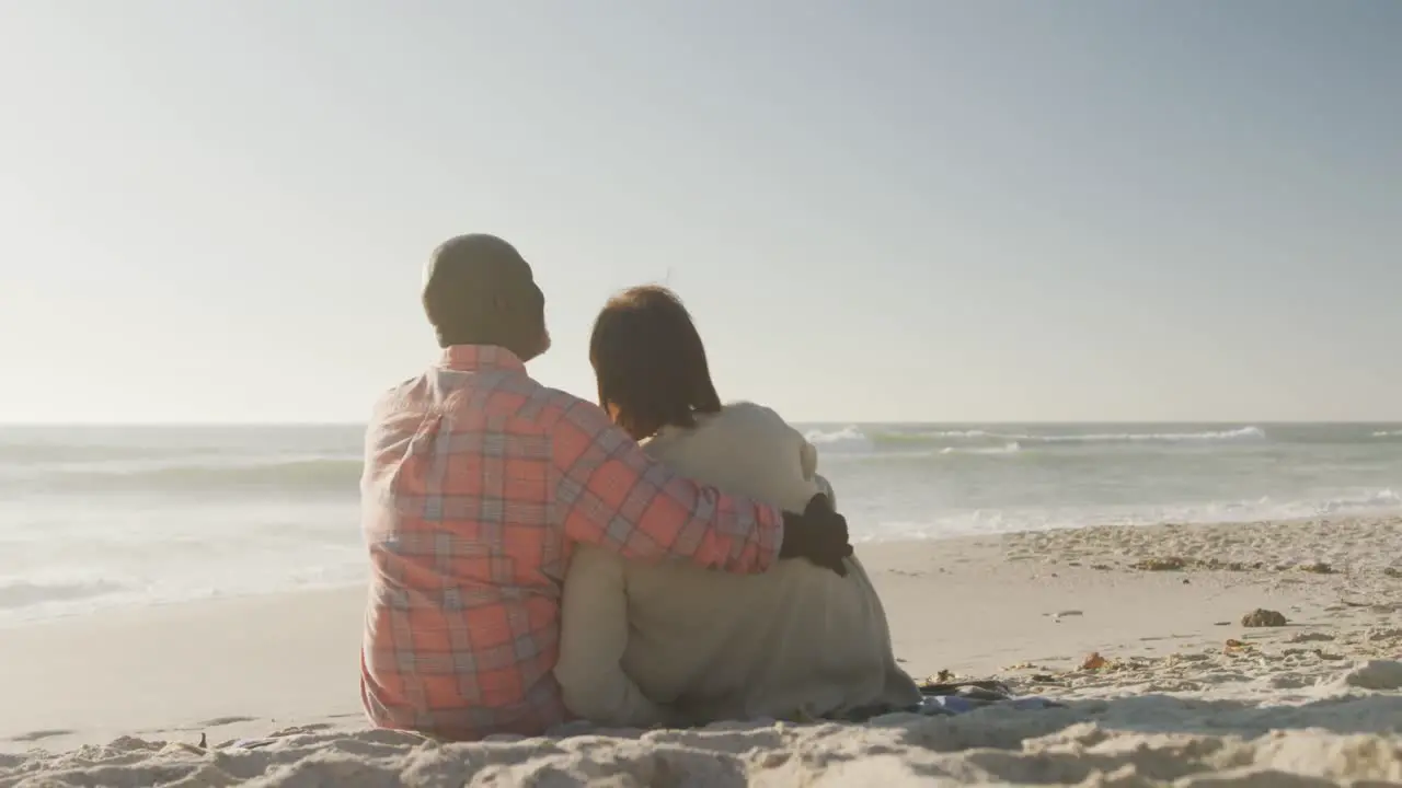 Smiling senior african american couple embracing and sitting on sunny beach