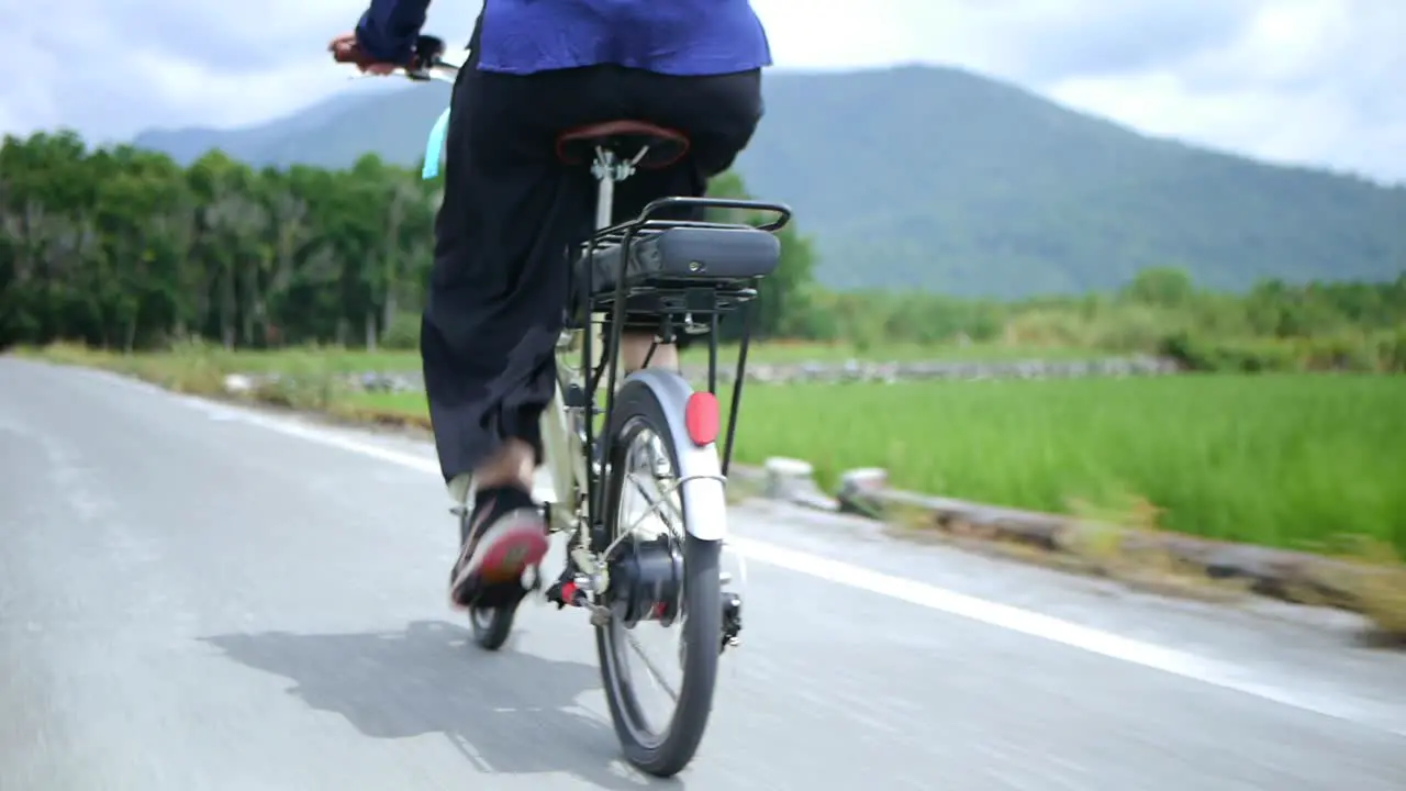 Asian woman riding bike during sightseeing trip through countryside filmed as medium shot following bicycle from backside of rider