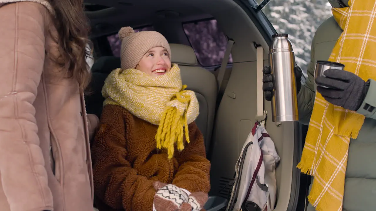 Teenage Girl Dressed In Winter Clothes Sitting In The Trunk Of A Car While Talking With Her Parents