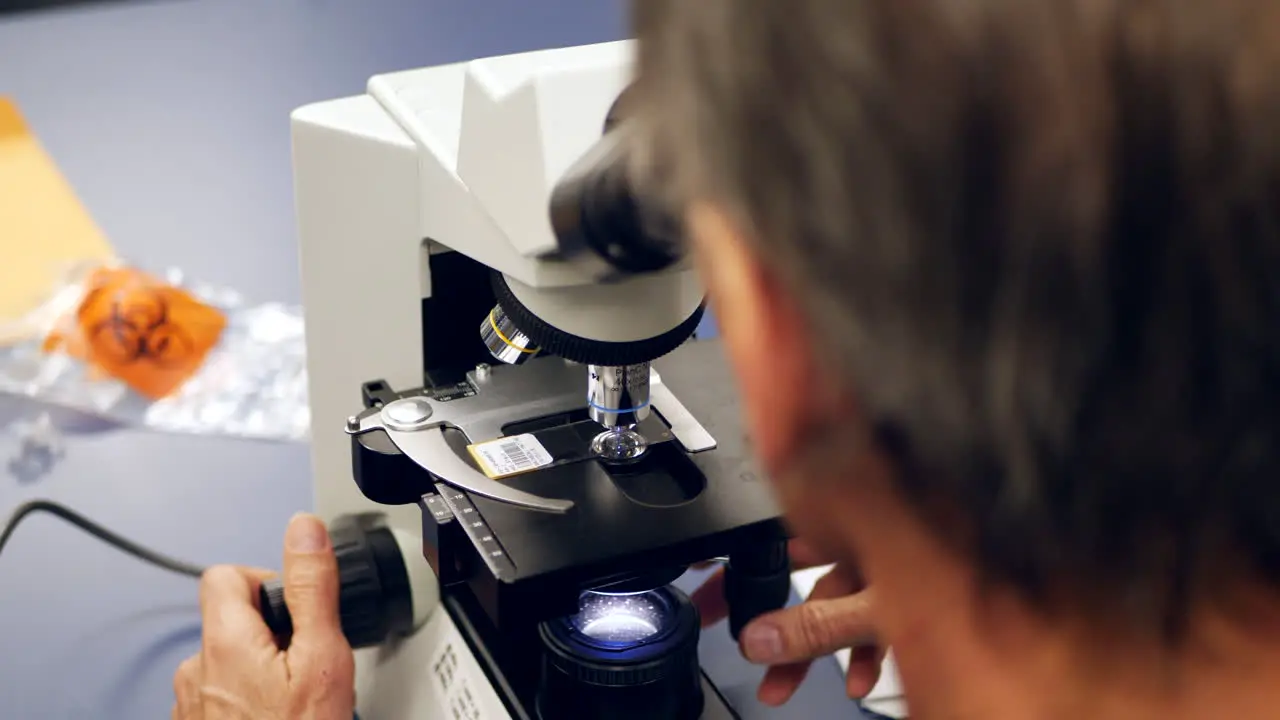 A scientist examining a slide with human cancer cells through a microscope in a medical research laboratory