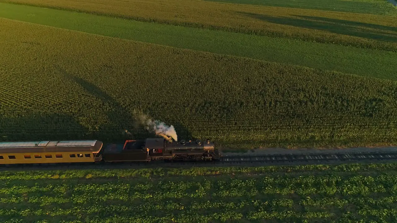 An Aerial View of A Steam Passenger Train Approaching Passing Thru a Corn Maze and Corn Fields During the Golden Hour on a Summer Day