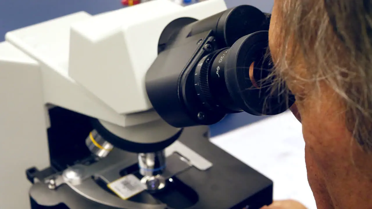 A scientist looking through the lens of a microscope at human cancer cells in a medical biology research laboratory