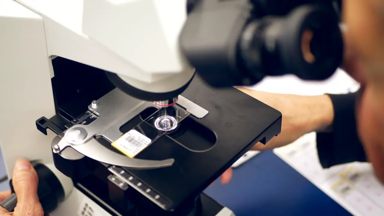 A scientist focusing on a slide of cancer cells from a medical biopsy on a microscope in a medical research science lab