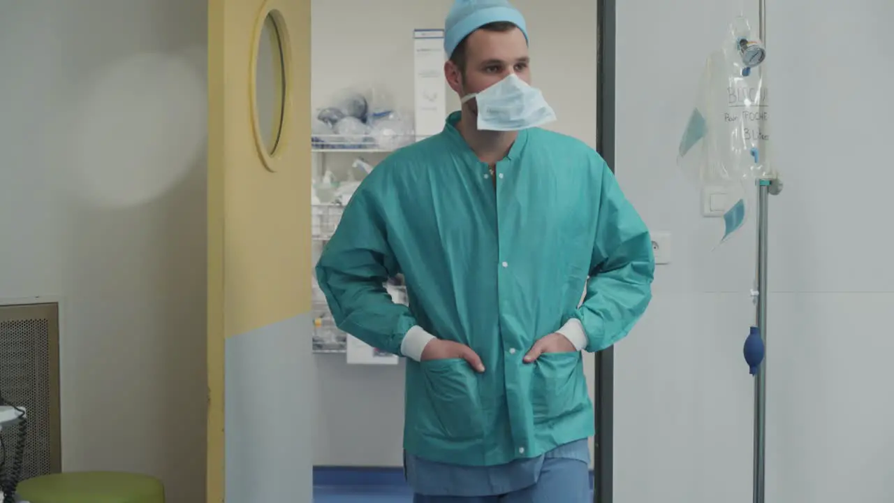 A doctor dressed in a professional suit wearing a surgical cap and a mask emerges from the doors