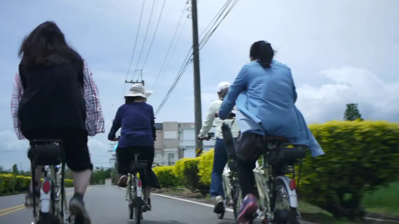 Group of female bikers riding on countryside road next to power lines filmed from backside following riders