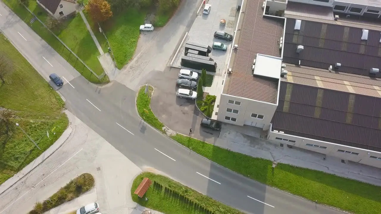 A cinematic view of car crossing the road from the top zooming in with an industry roof top and vehicles parked