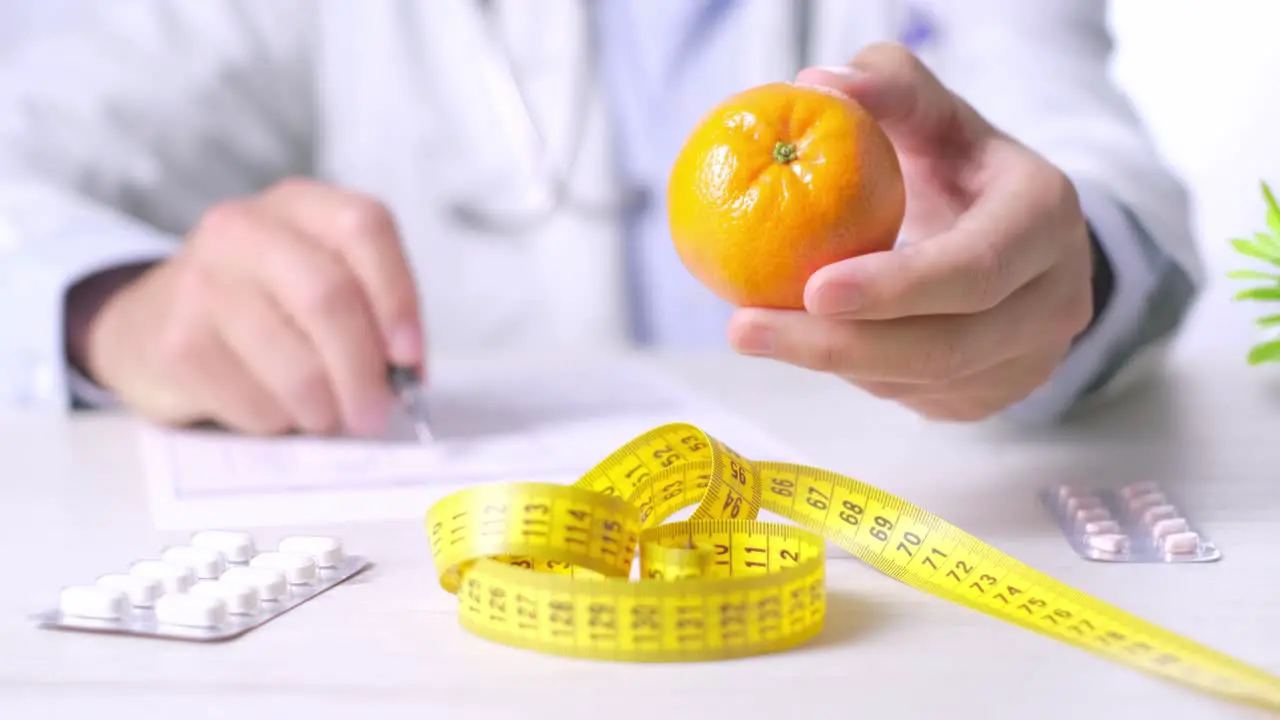 Doctor holding a tangerine and talking about healthy eating behavior and benefits Close-up