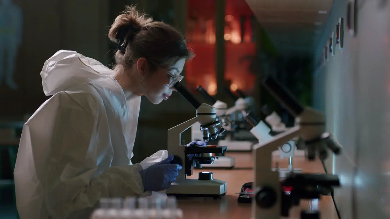 Female microbiologist analyzing sample with microscope in laboratory