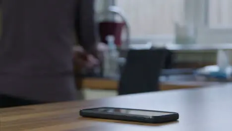 Sliding Close Up Shot of Phone On Kitchen Surface As Adult Cleans In the Background