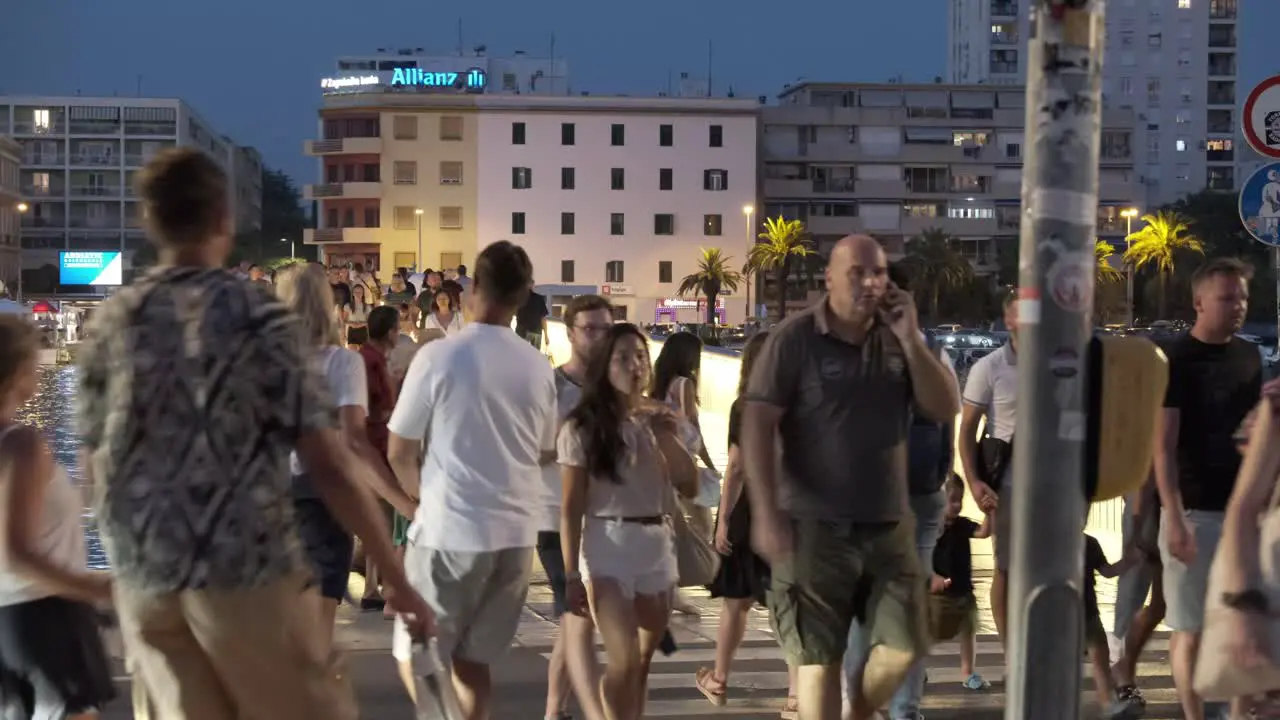 Night street pedestrian crossing at the bridge in Zadar Croatia with large crowds and water reflection and city buildings