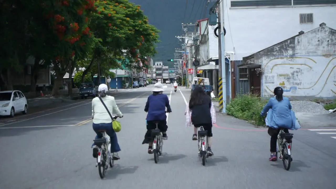 Group of 4 woman riding bikes through countryside town in Asia filmed from backside following riders