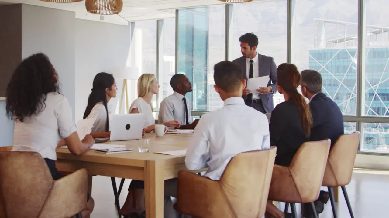 Businessman Stands To Address Meeting Around Board Table