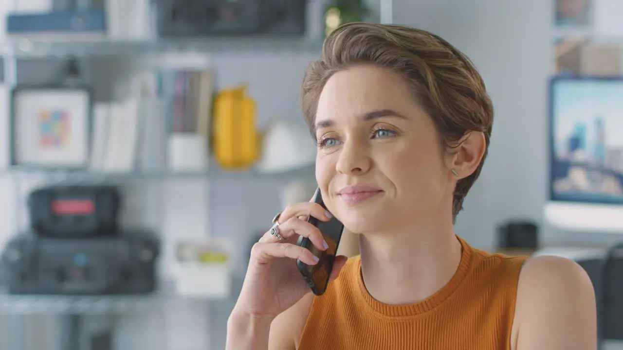 Close Up Of Female Architect In Office Working At Desk Taking Call On Mobile Phone