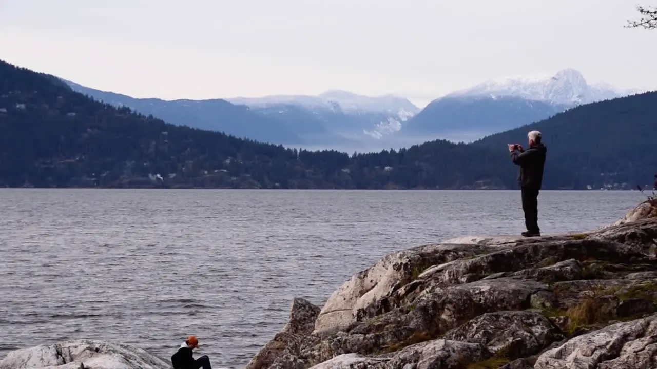 Older man takes photos from cliff of sea and mountains long shot