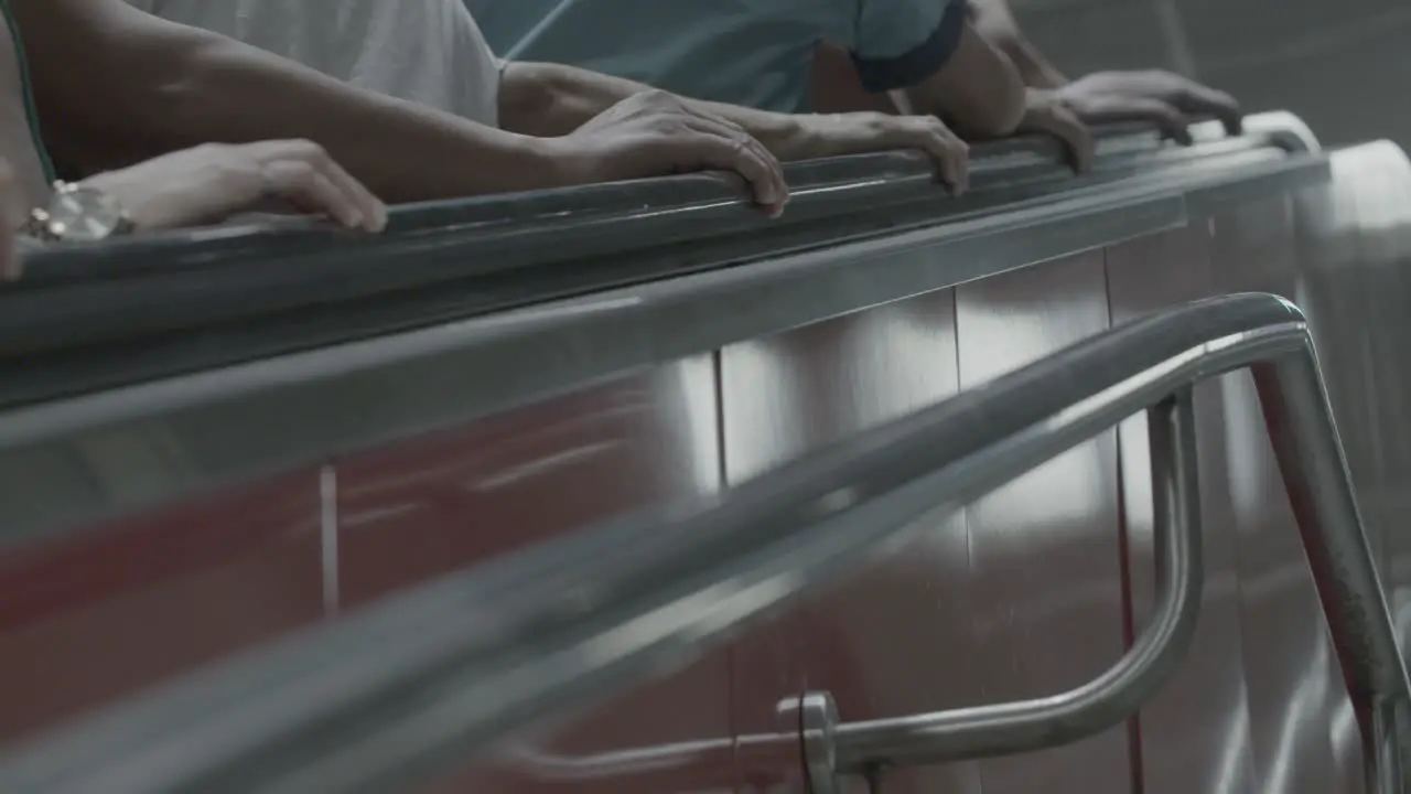 A medium shot of multiple people going up an escalator captured with a static camera showing only arms and hands in focus