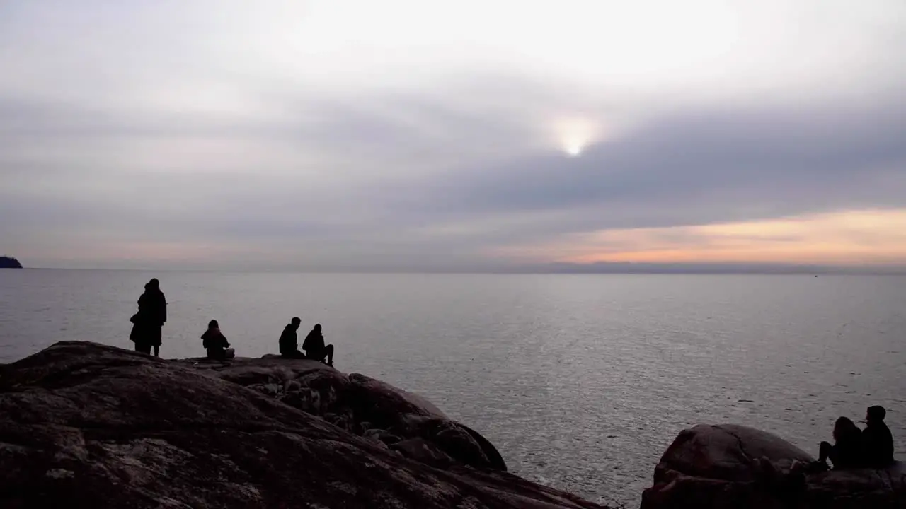 Silhouetted people hang out to watch sunset on coastline long shot