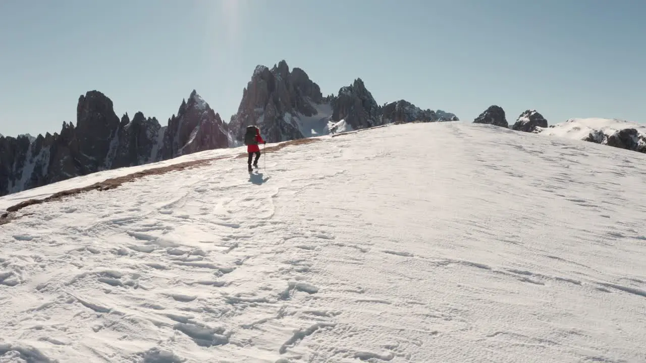 Wide circling drone shot of trekker walking along snowy ridge with Candini mountains in the background