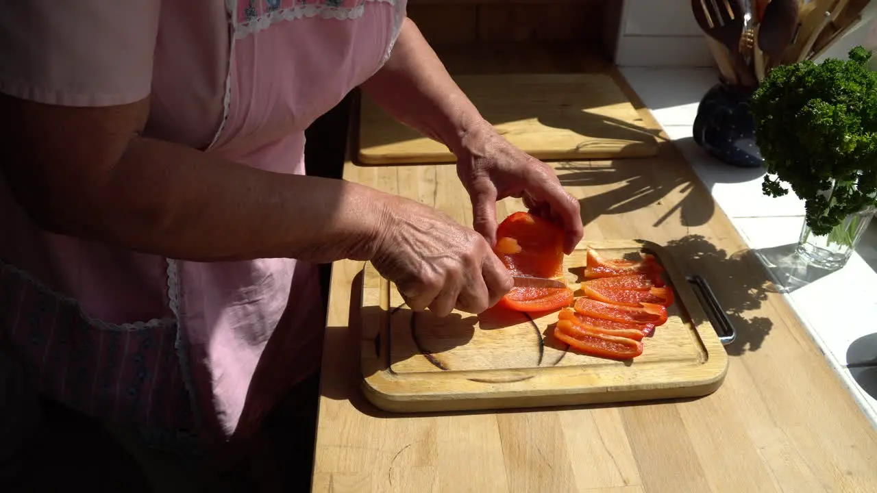 Senior lady cutting paprika in the kitchen on a sunny afternoon