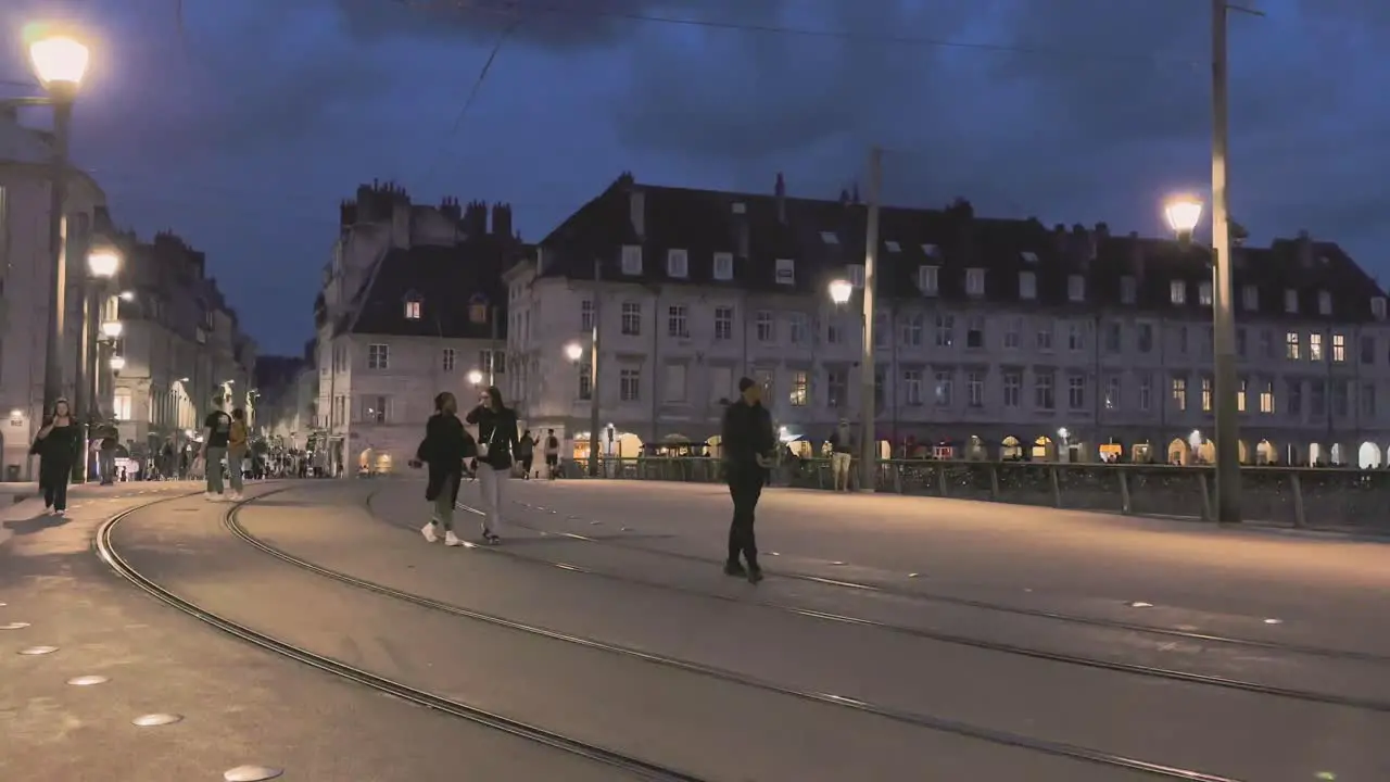 City Besancon in Franche-Comté night life with people walking over pedestrian bridge with tram tracks and streetlights