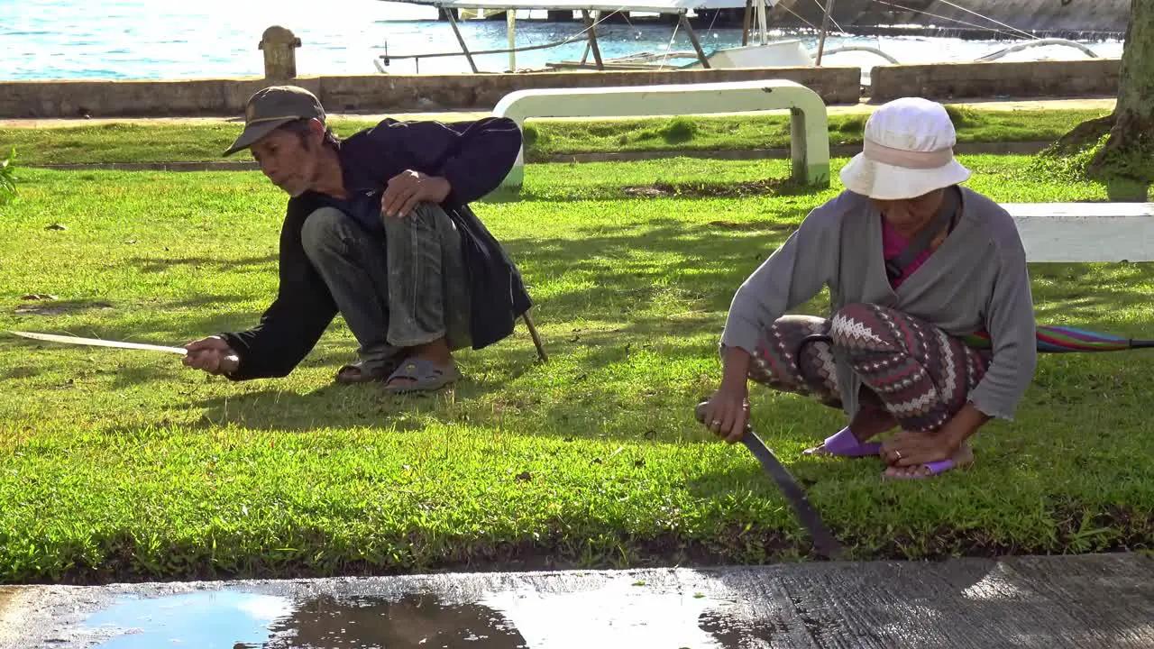 Two gardeners keep the grass short using machetes along the boulevard of Cagbianao Dinagat Philippines