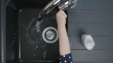 Top Down Shot of Young Childs Hands Turning On Kitchen Tap