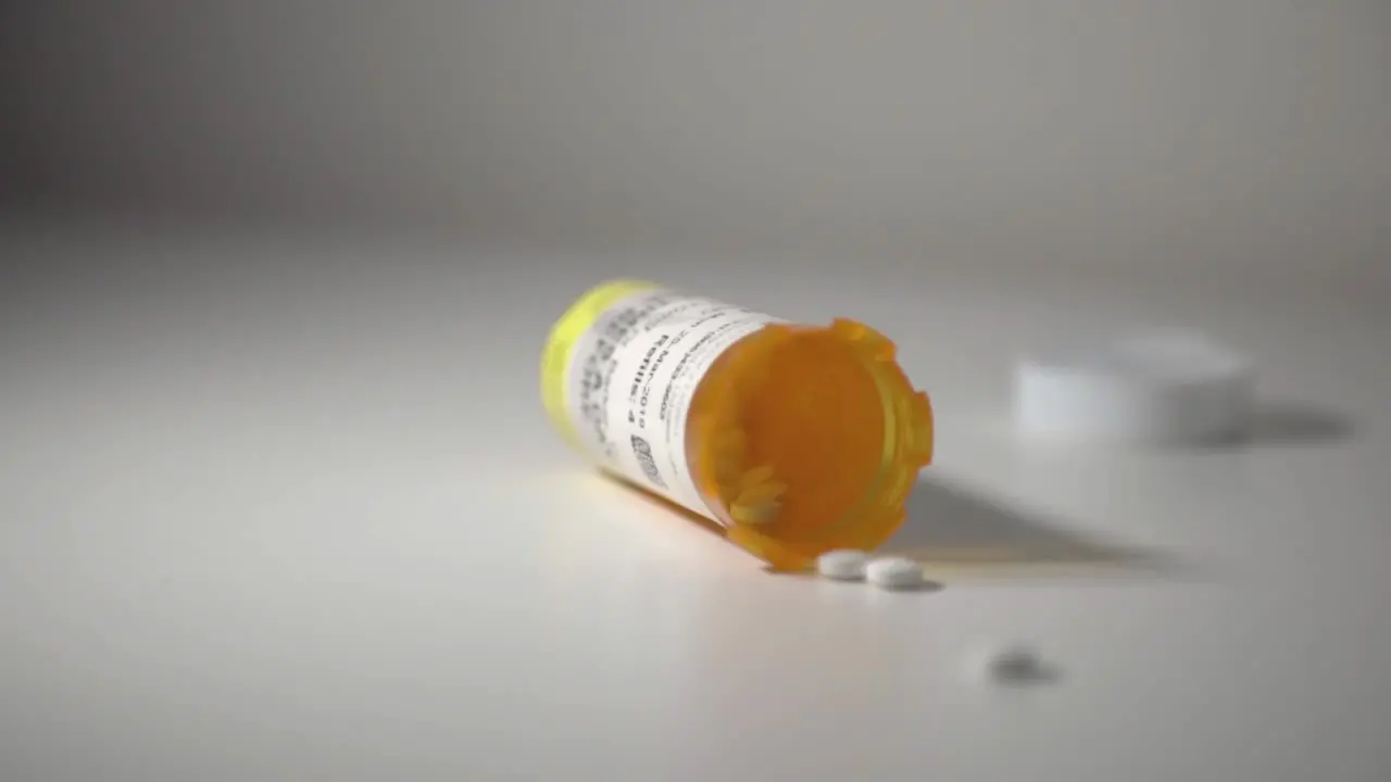 White Pills Spilling Out Of A Toppled Yellow Pill Bottle On Top Of A White Table