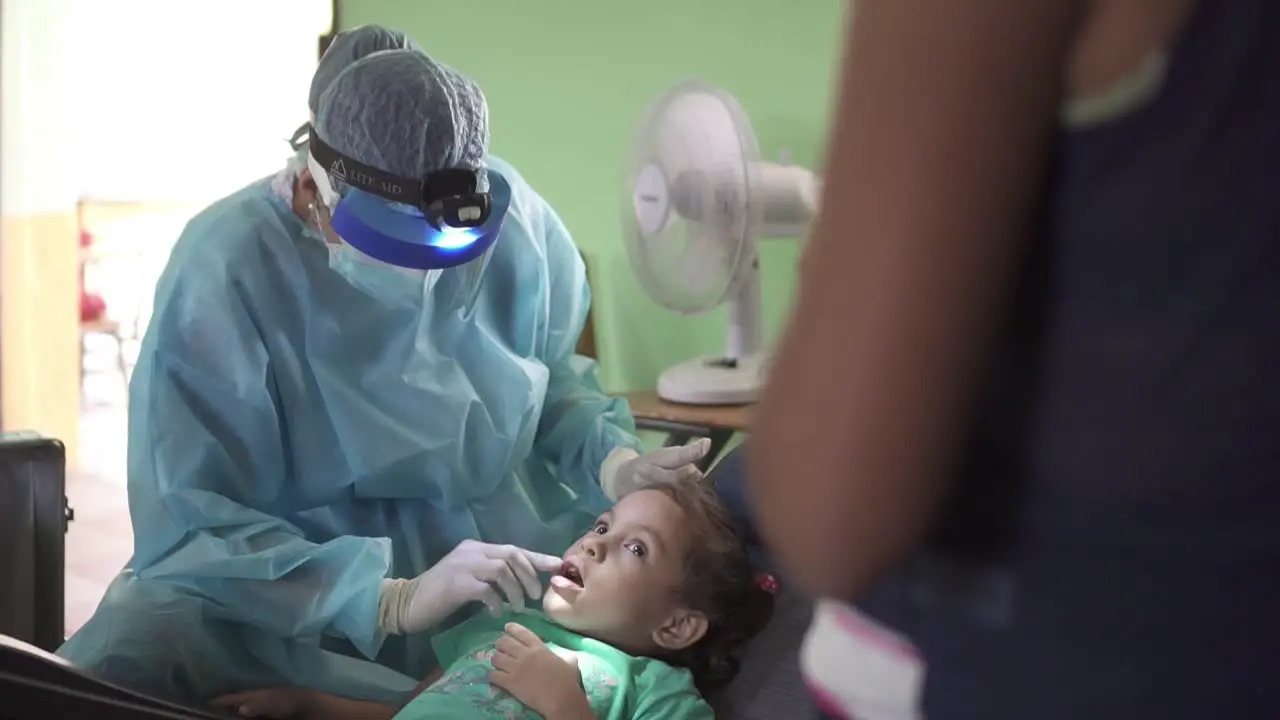 Dentist woman checks the mouth of a little girl during a medical brigade in an improvised clinic in a poor community school