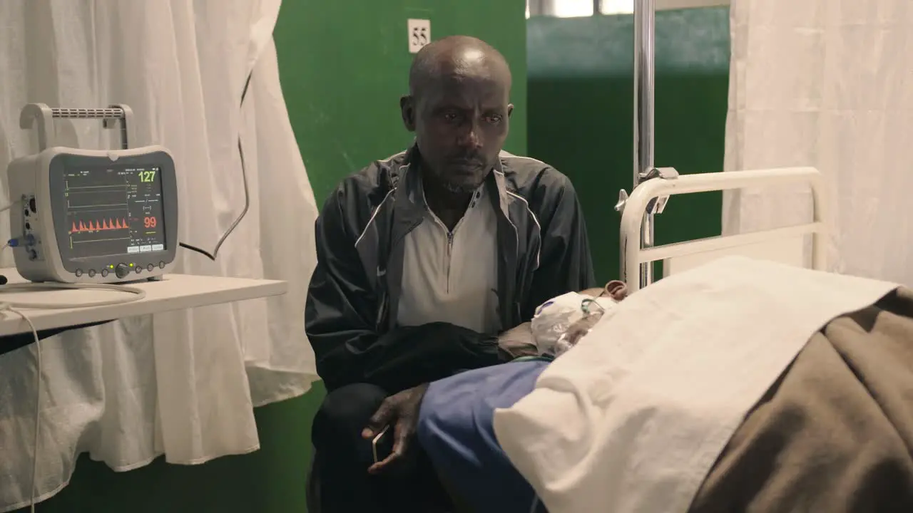 Father sitting next to his son on a hospital bed in a clinic after eye surgery with a heart monitor next to them