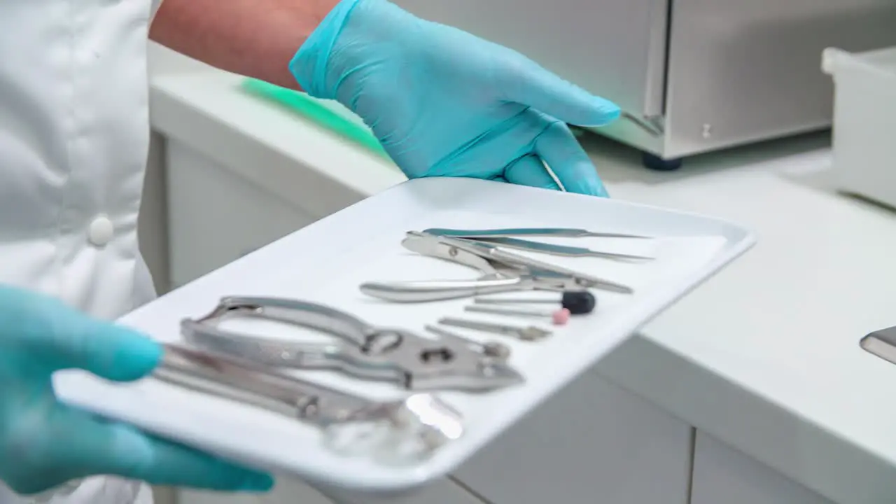 Medical professional holding instruments on tray wearing blue latex gloves