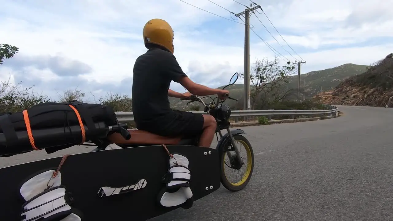 Man rides motorbike transporting surfboard and kitesurfing equipment