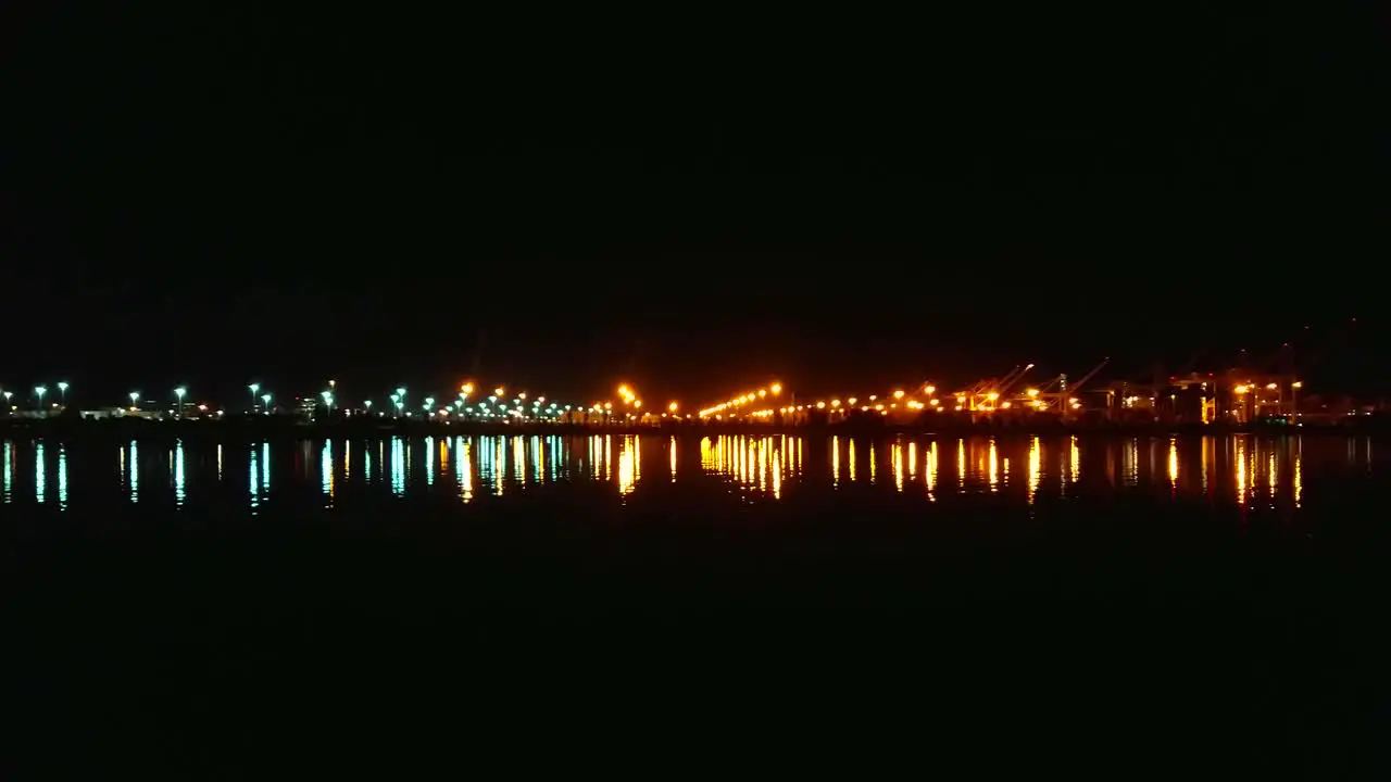 A slow pan to the right across the glistening waters with lights from the bay shipping industry