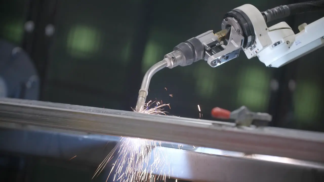 Footage of sparks falling off a steel frame while a robotic welder is working on it