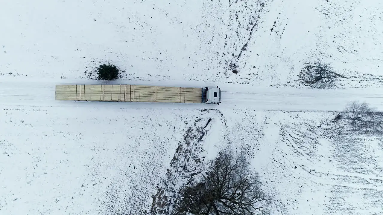 Aerial top down shot of long truck transporting Cleared wooden tree trunks on snowy winter day