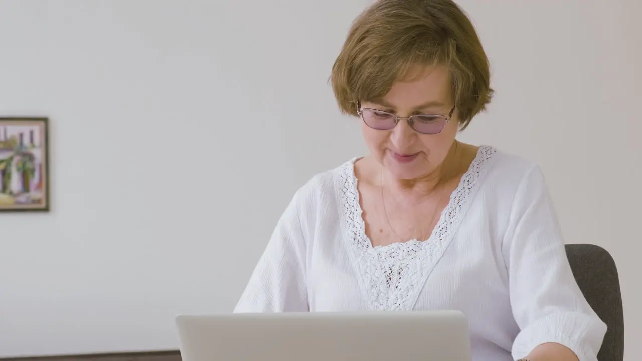 Senior Woman With Eyeglasses Sitting On A Sofa Using Tablet