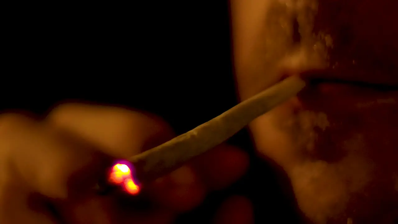 4K closeup of Caucasian male smoking cannabis spliff joint during night