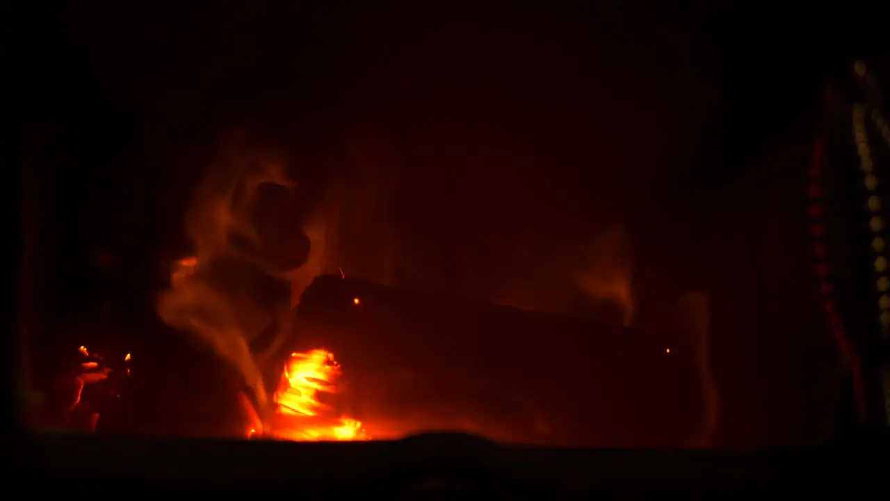 Slow motion household home log fire burning wood with orange flame and hot embers with dark background close up shot flicking flames